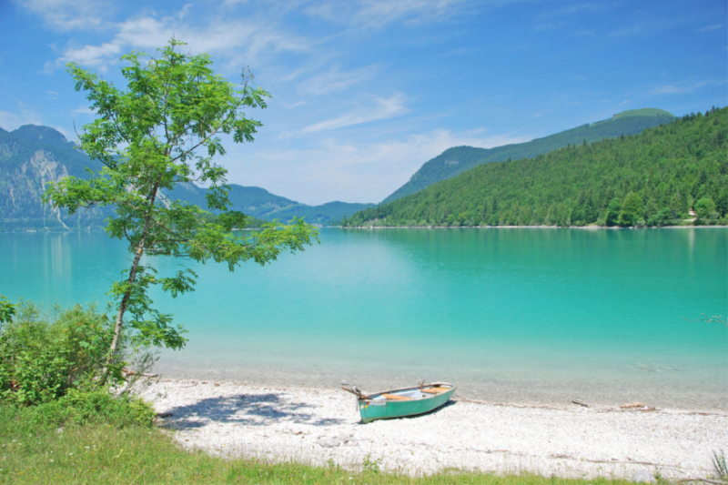 Türkisblauer Walchensee mit Boot am weißen Kieselstrand