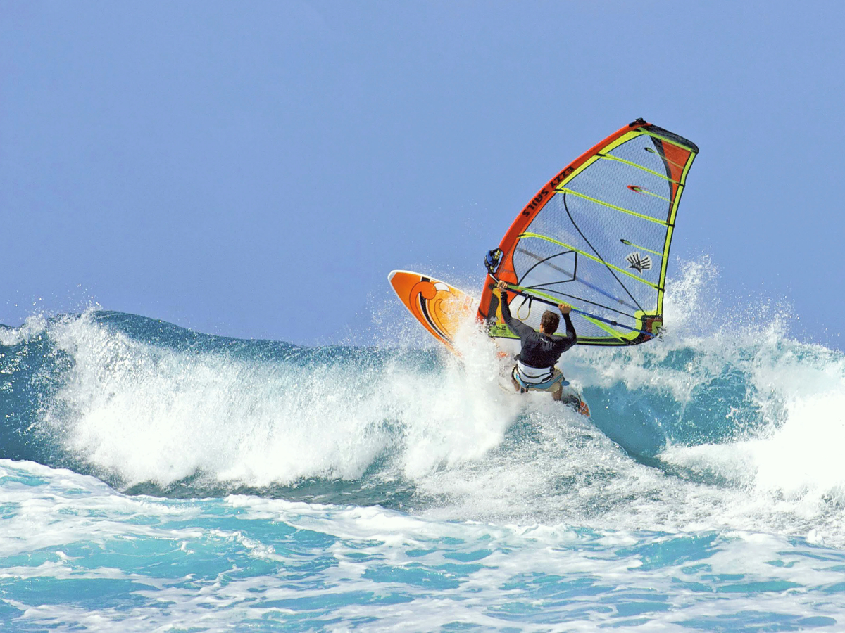 Beherzter Windsurfer gleitet rasant durch die Brandung.