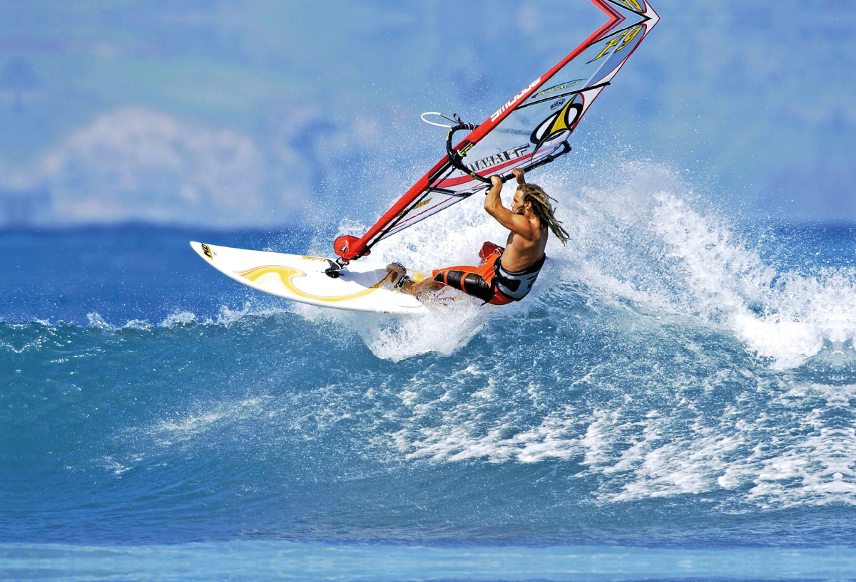 Athletischer Windsurfer dreht das Board auf dem Wellenkamm.