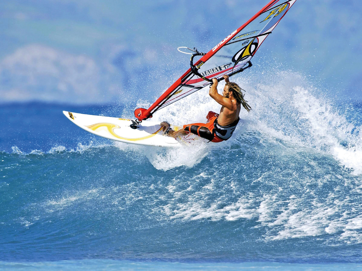 Athletischer Windsurfer dreht das Board auf dem Wellenkamm.