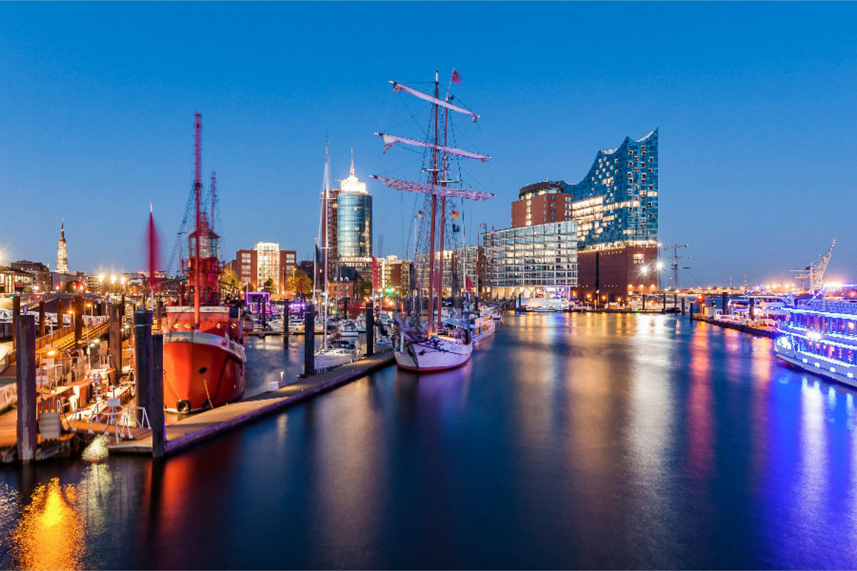 Ausflugsboote und die Elbphilharmonie in der HafenCity in Hamburg bei Nacht.