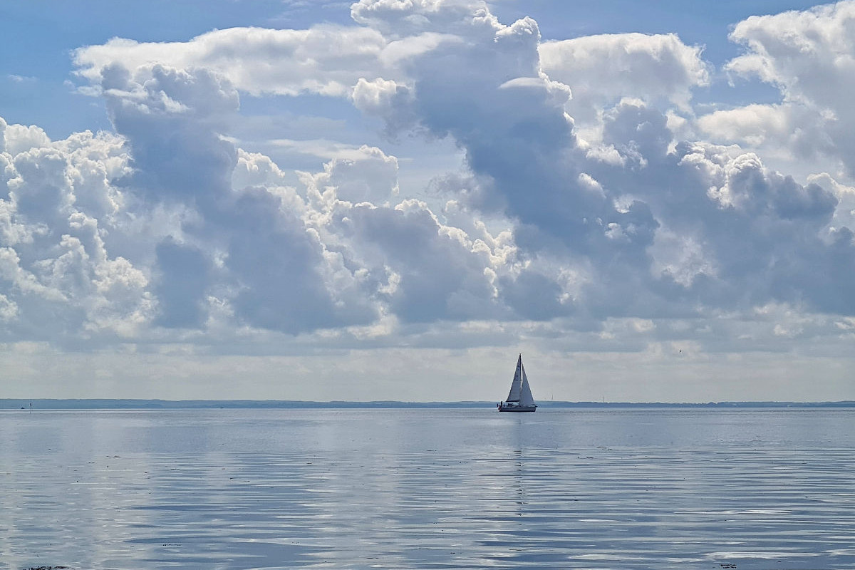 Segelboot am Horizont mit Wolkenspiegelung am Strand Grömitz