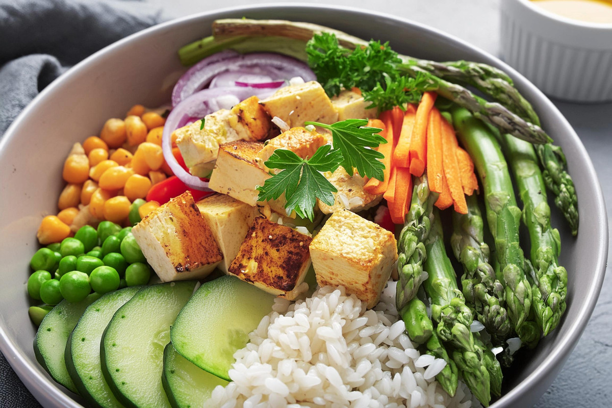 Vegane Bowl mit grünem Spargel, Tofu, Karotten, Gurken, Reis, Toppings, Dressing,