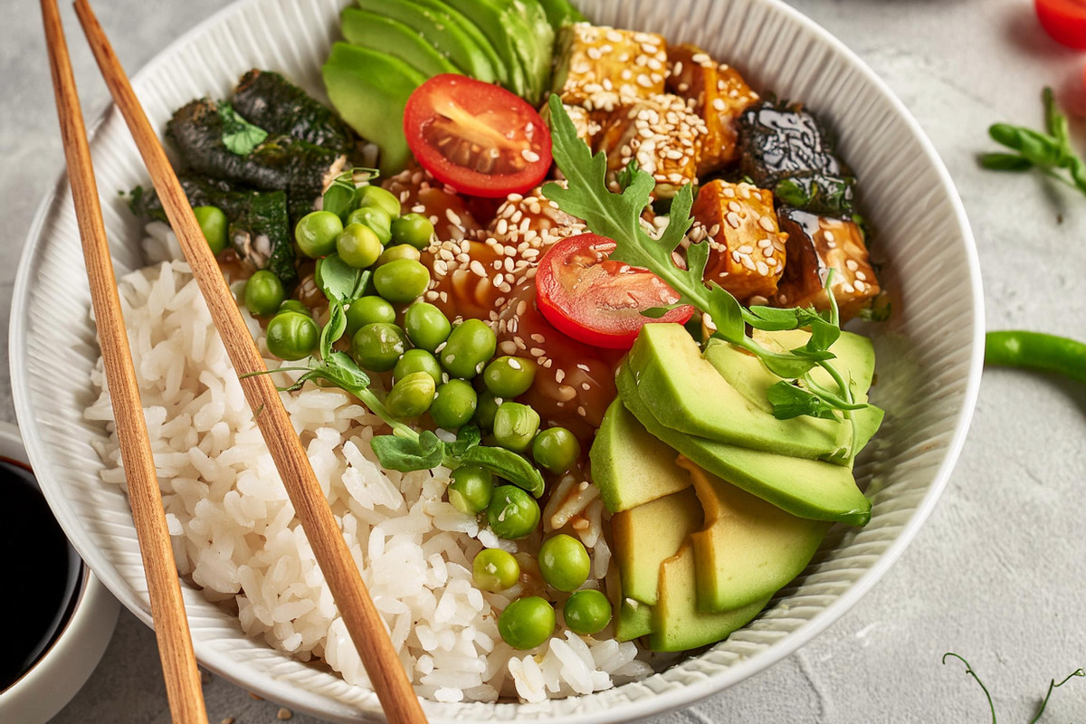 Vegane Bowl mit Erbsen, Poke Reis, Tomaten, Algen und Avocado, Tofu, Basilikum, Toppings und Dressing