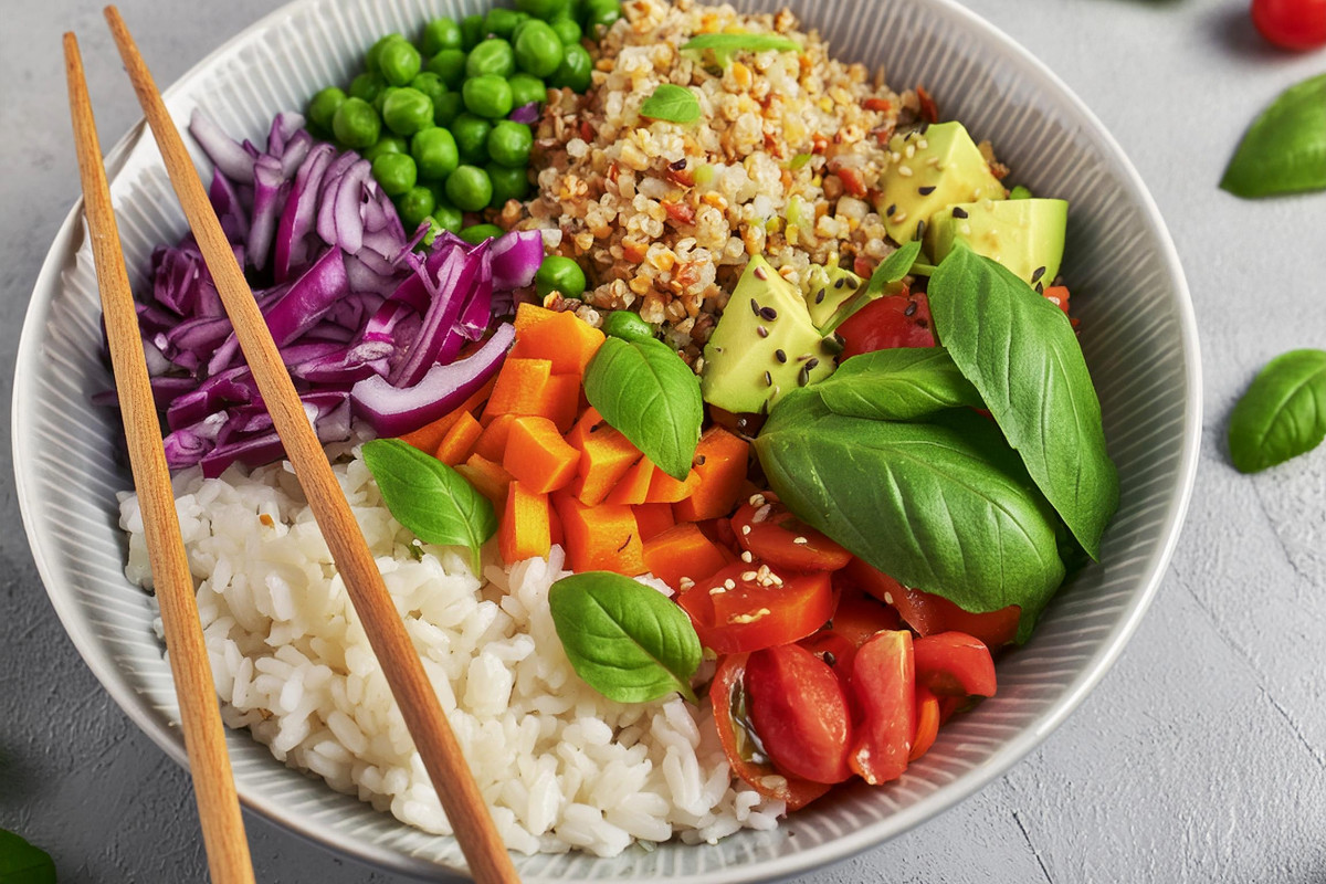 Vegane Bowl mit Reis, Rotkohl, Karotten, Tomaten, Erbsen, Basilikum