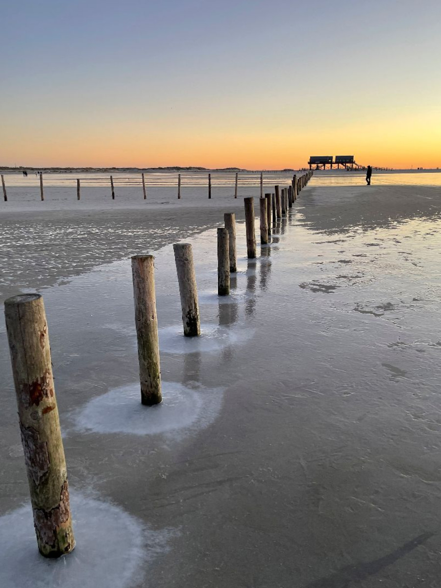 Runde Eisformationen umsäumen eine  Pfahlreihe am Ordinger Strand