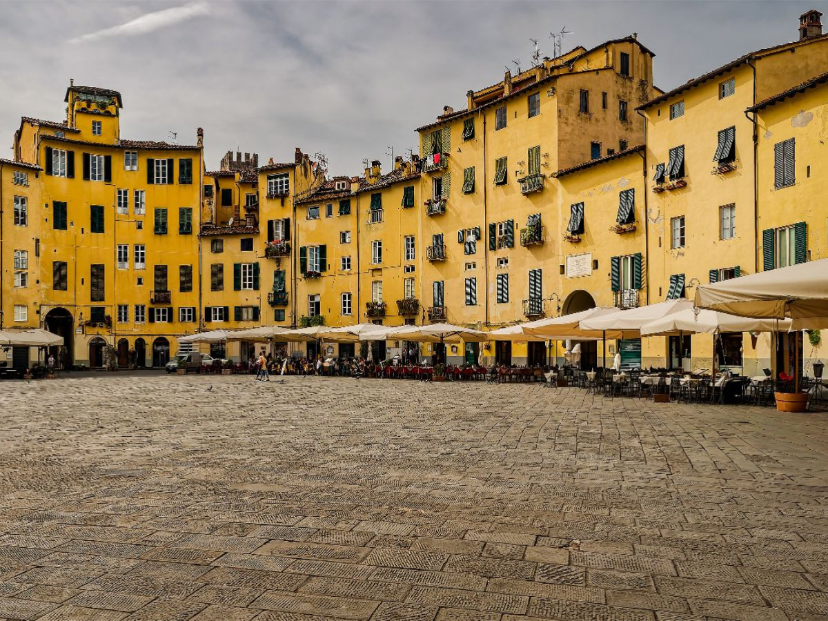 Lucca: Die einzigartige, elliptische Piazza dell'Anfiteatro mit ihren charakteristischen ockergelben Häuserfronten und einladenden Straßencafés
